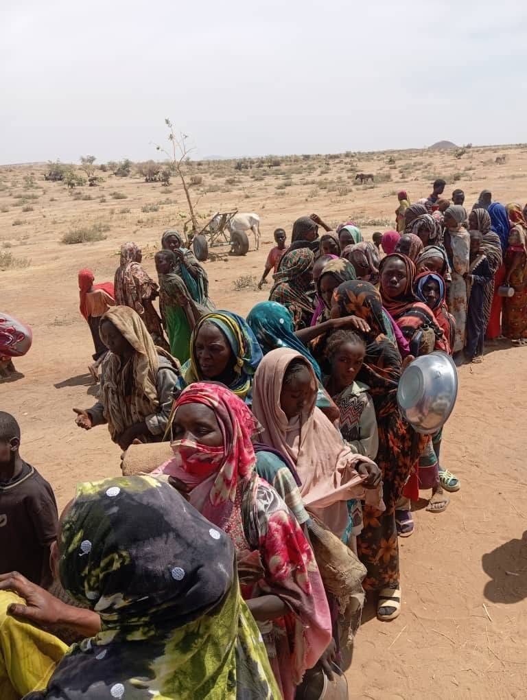 Women and children queue with bowls for a meal in North Darfur